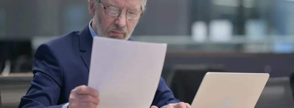 Empresário segurando uma folha de papel e pagando multa em seu notebook